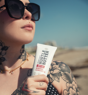 Person holding a tube of Hustle Butter sunscreen with a desert background